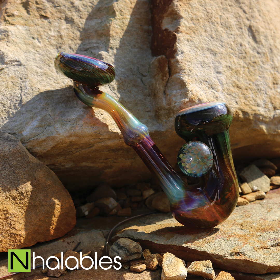 Nhalables Social Post Showing a Serendipity Sherlock by Akron Based Artist Eyehole Glass Sitting on a Rock in the Sun.