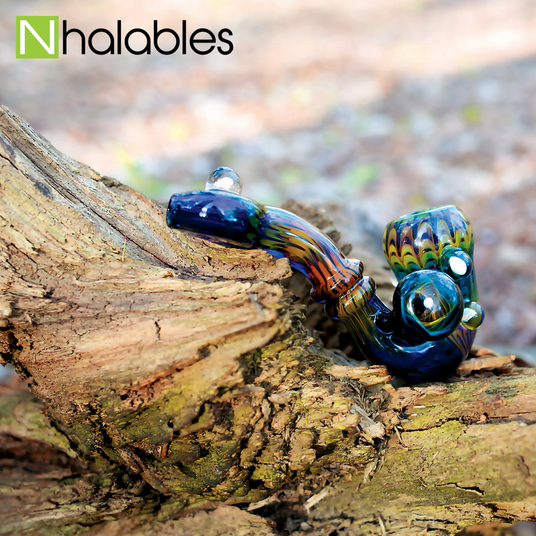 Nhalables Social Post showing a Sharon, Ohio artist Harry Marbleman's opal studded fumed sherlock hand pipe sitting on a tree stump 