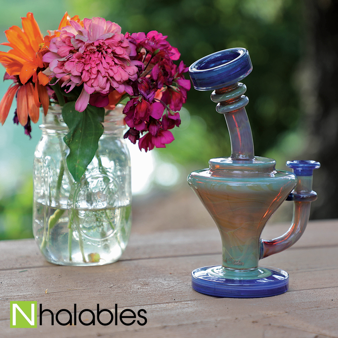 Nhalables Social Post Showing an Experimental Green Strike mini Viral Oil Rig by Zombie Hand Studios sitting on a wooden table next to a jar of flowers.