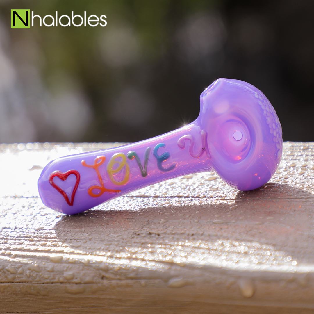 Nhalables social post for "Love You spoon/Handpipe" by Michigan Based Glassblower "White Chocolate Glass" sitting on a wet wooden railing with some blurry trees behind it