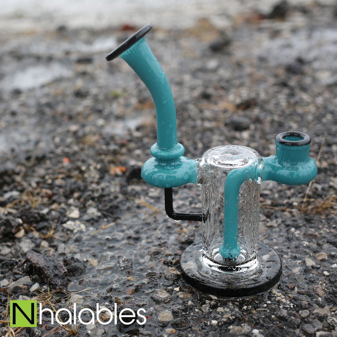 Nhalables Social Post showing a Teal Colored Amporphous Glass Rig Sitting on the asphalt in the rain.